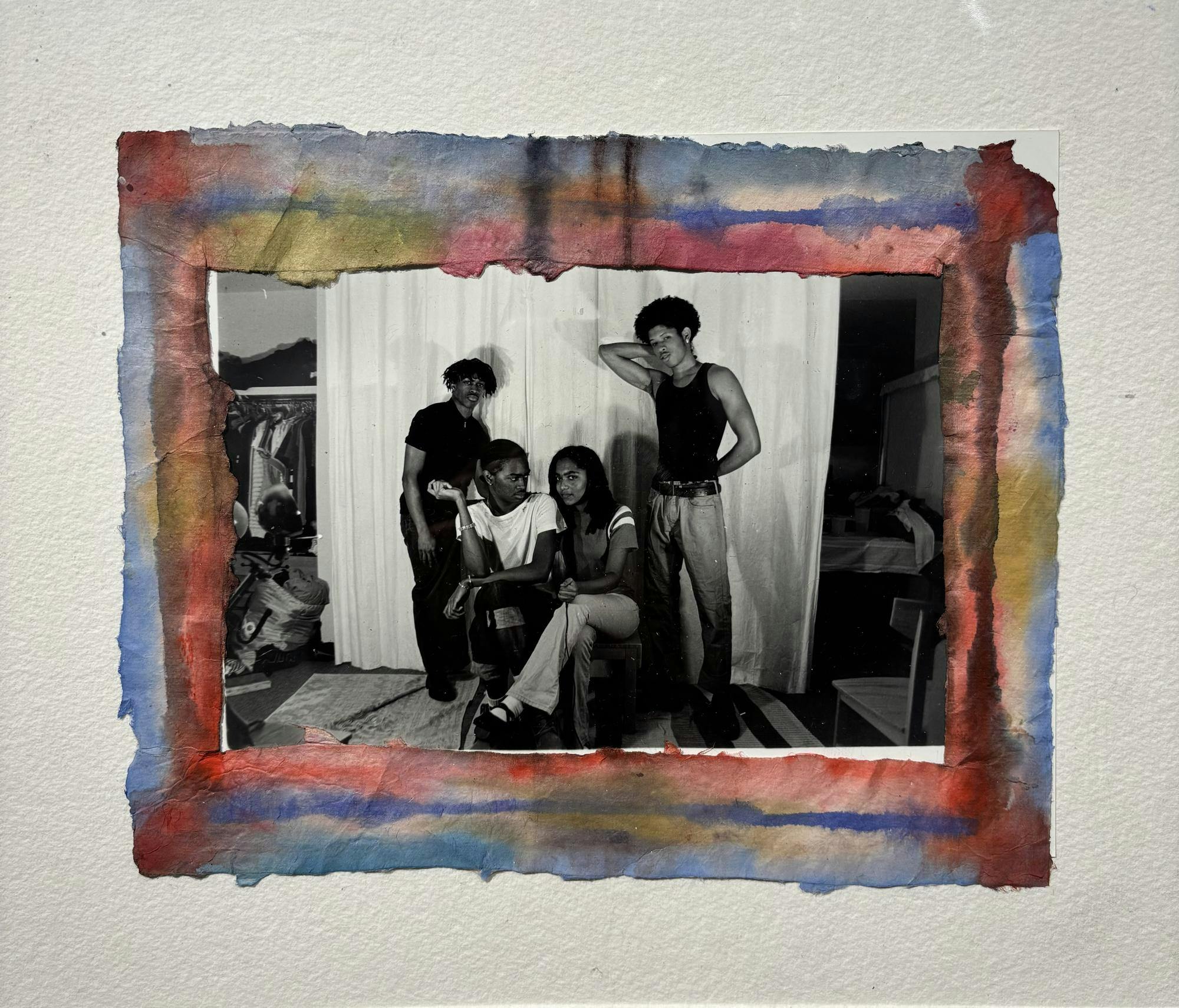 A black and white photograph of four individuals -- two standing and two sitting -- is surrounded by a colorful border. 