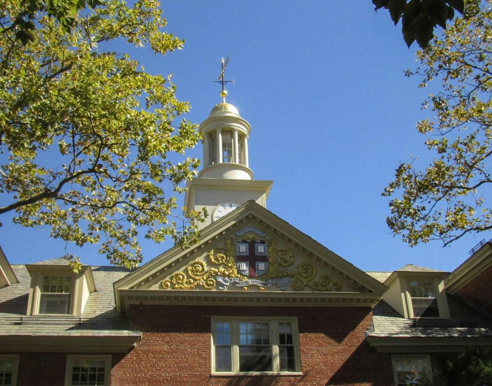 Photo showing the roof of Wriston arch: The top of a brick building with the Brown shield logo on the front and a white clock tower above.  