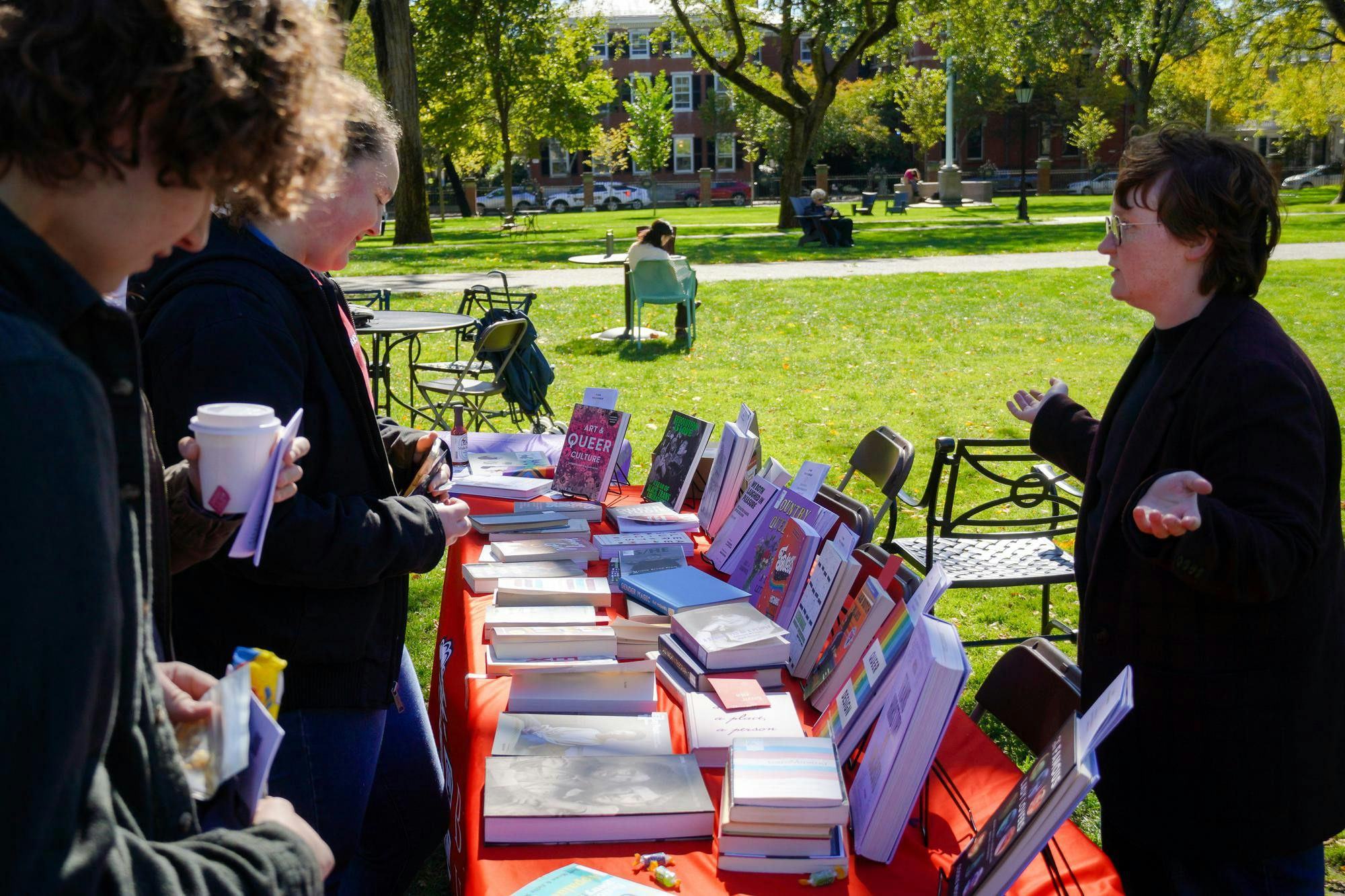 Photo of students looking at books on a table on the Main Green and talking to event organizers.