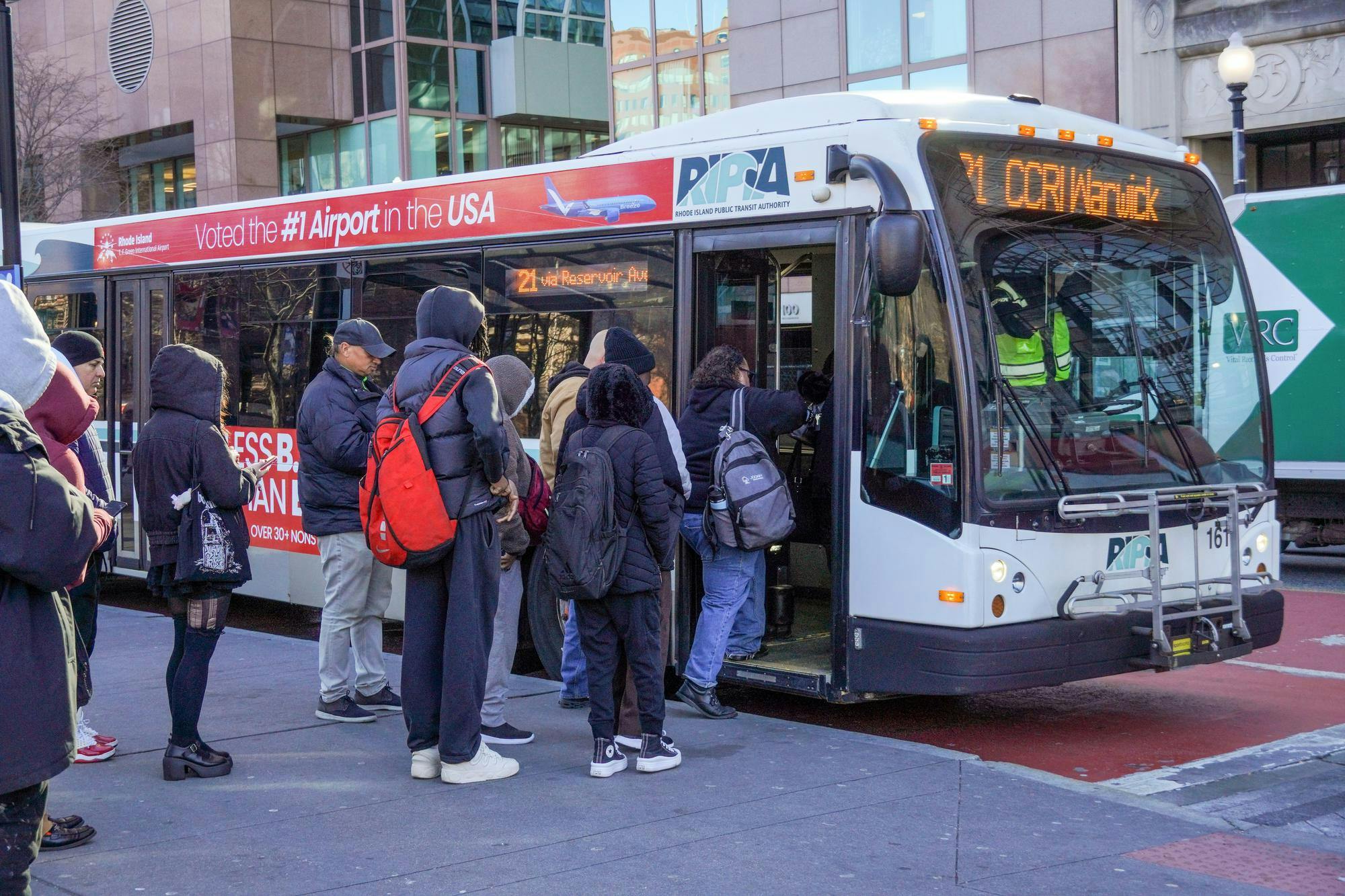 Photo of a RIPTA bus in Kennedy Plaza destined for CCRI Warwick, with a long line of riders waiting to board.