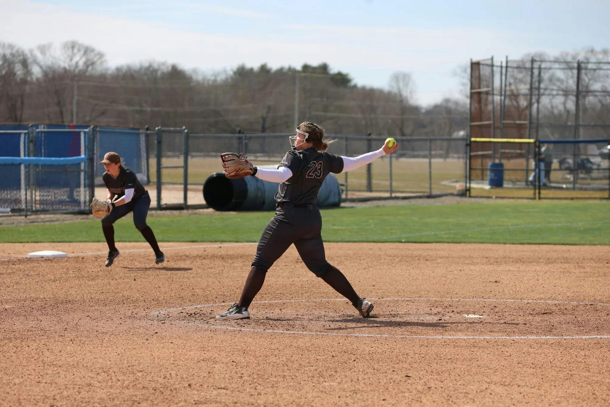 A softball player outstretches her arm mid-pitch. 

