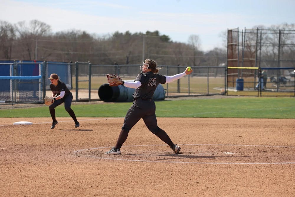 A softball player outstretches her arm mid-pitch. 

