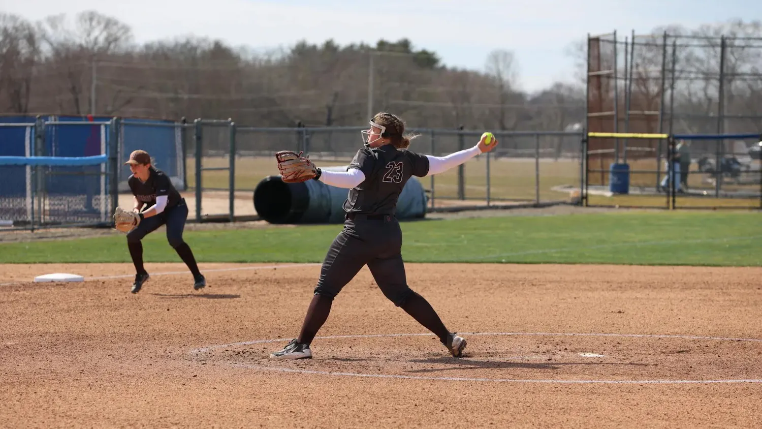 A softball player outstretches her arm mid-pitch.