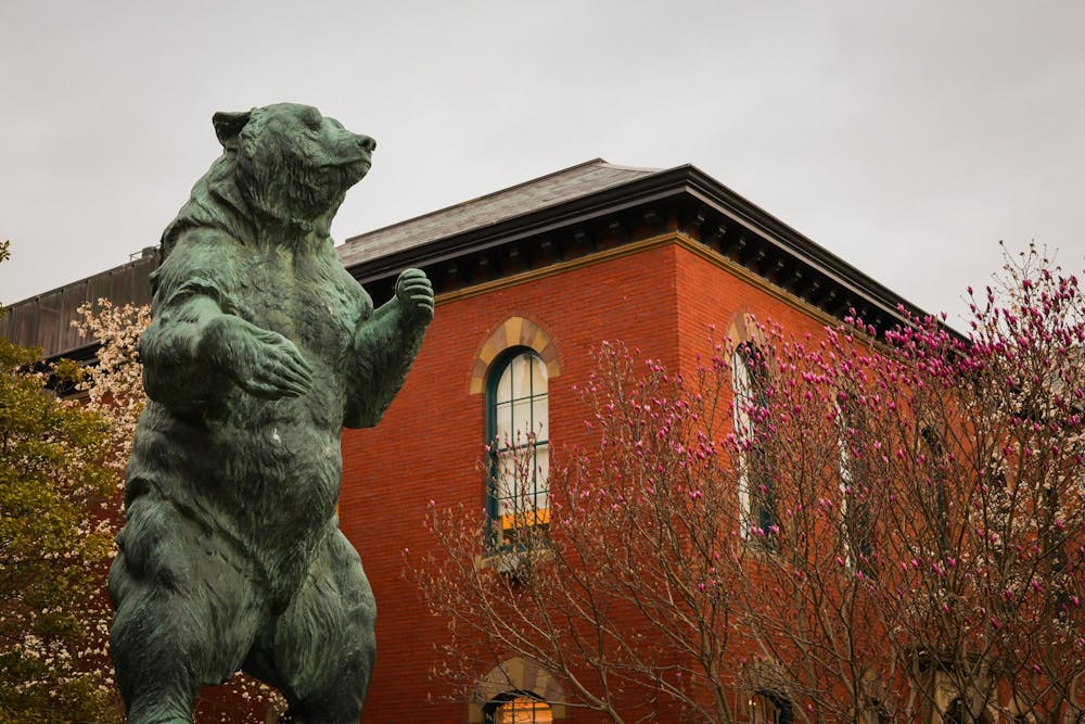 Brown University's Bear statue with the Salomon Center, a brick building, and trees in the background.