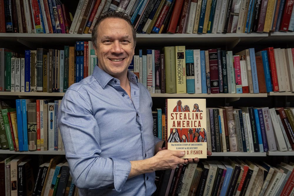 A photo of Professor Linford D. Fisher holding his book “Stealing America” in front of a bookshelf. 