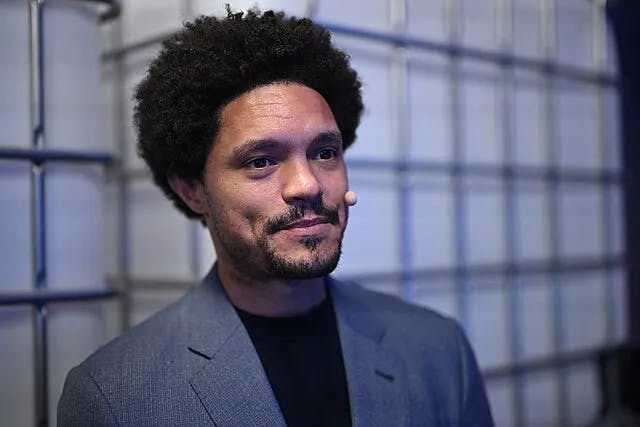 A close-up photo of Trevor Noah smiling in a gray suit. 