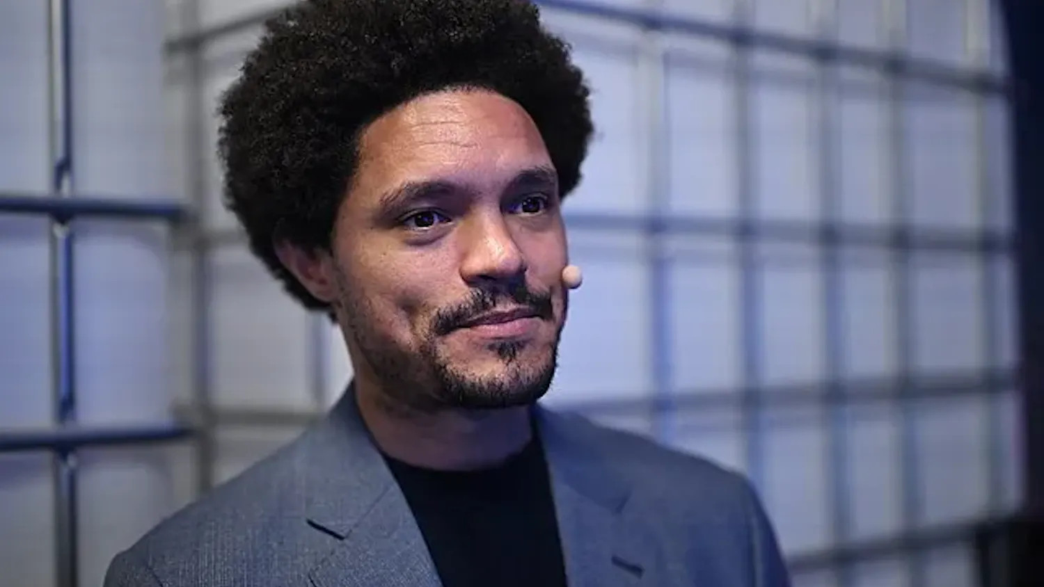 A close-up photo of Trevor Noah smiling in a gray suit.