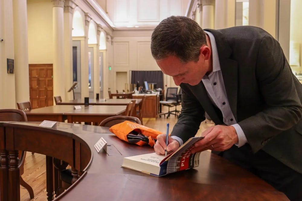 Photo of Professor Seth Rockman leaned over signing a copy of his book Plantation Goods.