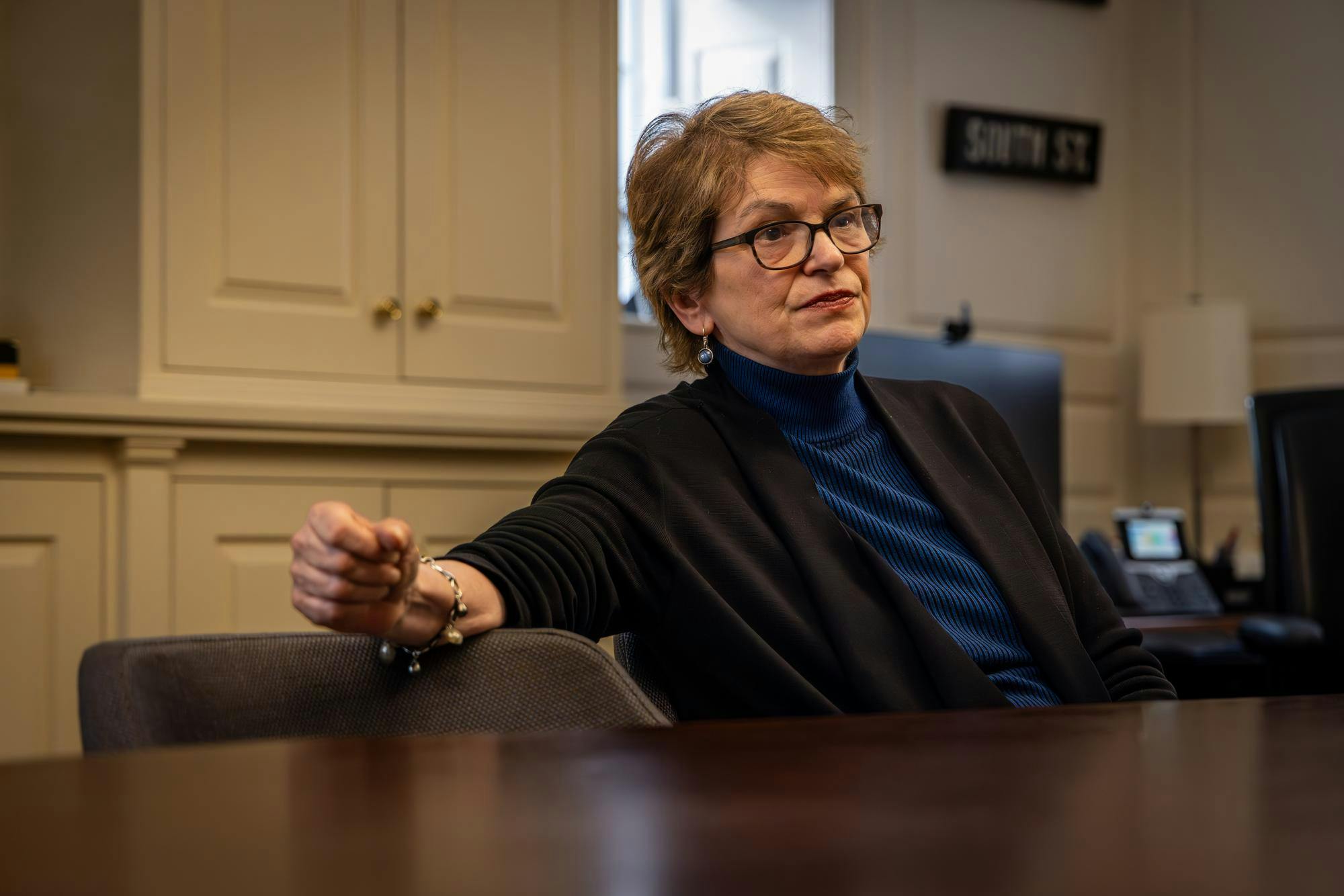 A woman with short hair sits at a table in a blue shirt.