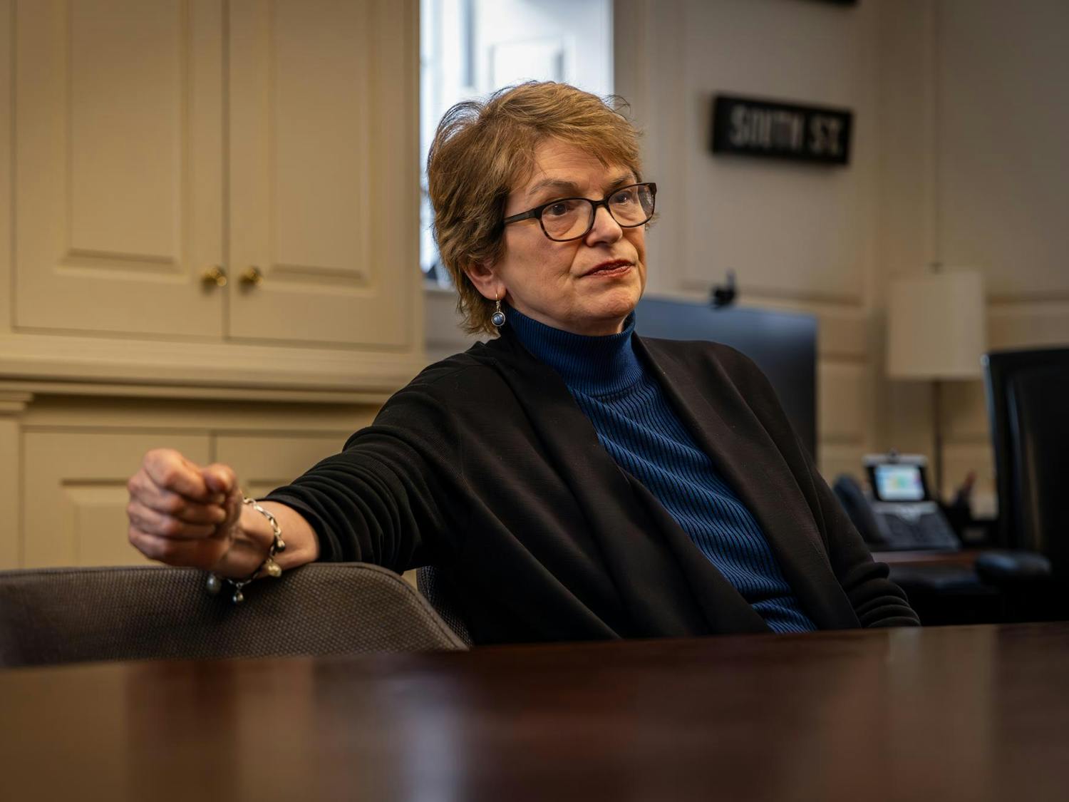 A woman with short hair sits at a table in a blue shirt.