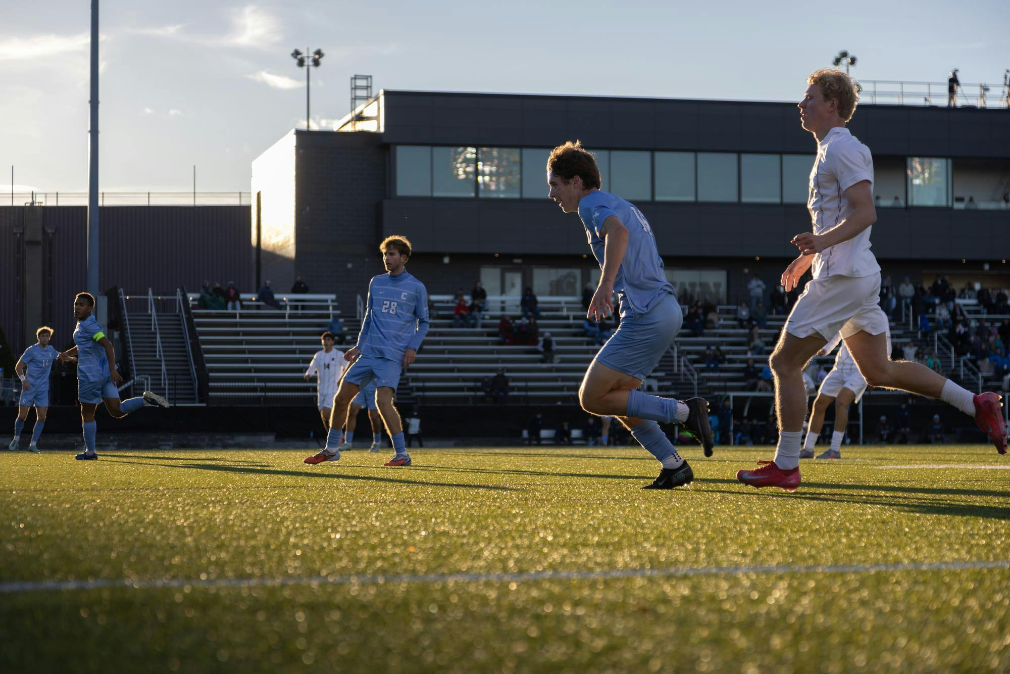 Brown and Columbia soccer players running down a soccer field on a sunny afternoon.