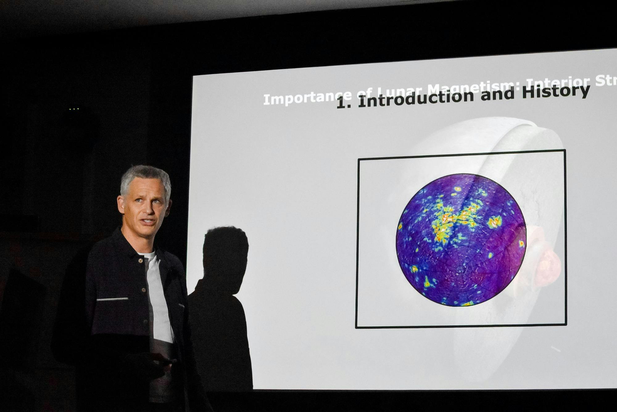 Thomas A. Mutch speaks in front of a projected slideshow.
