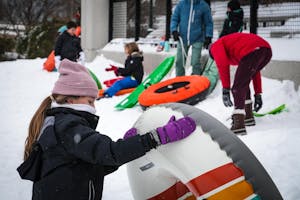 A little girl with a pink hat and black jacket holds a snow tube.