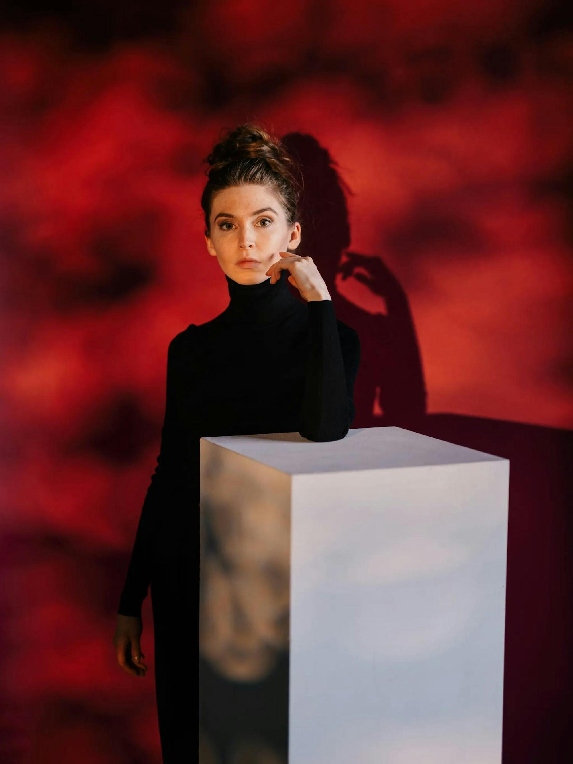 Photo of Jeannette Andrews wearing a black dress against a bright red background. 
