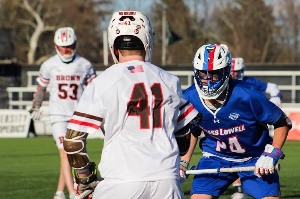 Photo of a Brown lacrosse player facing off against a University of Massachusetts at Lowell player.