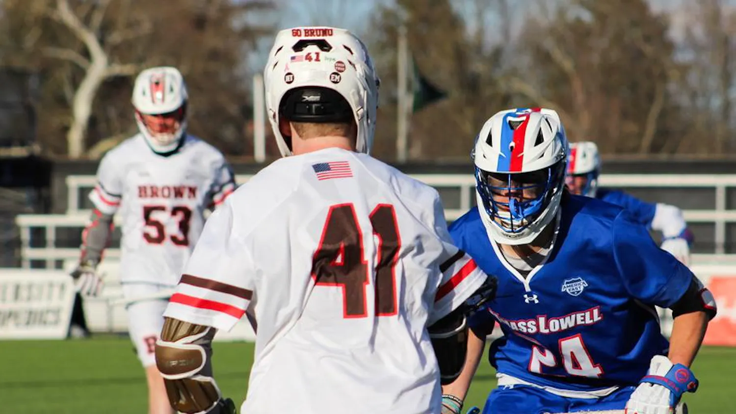 Photo of a Brown lacrosse player facing off against a University of Massachusetts at Lowell player.