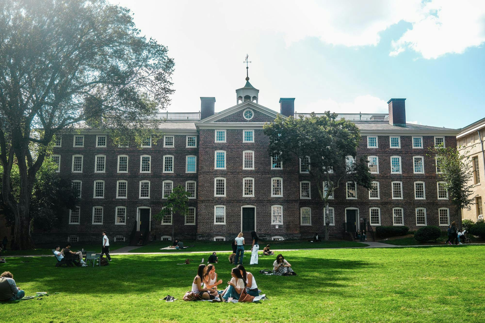 A photo of students talking on the Main Green in front of University Hall. 