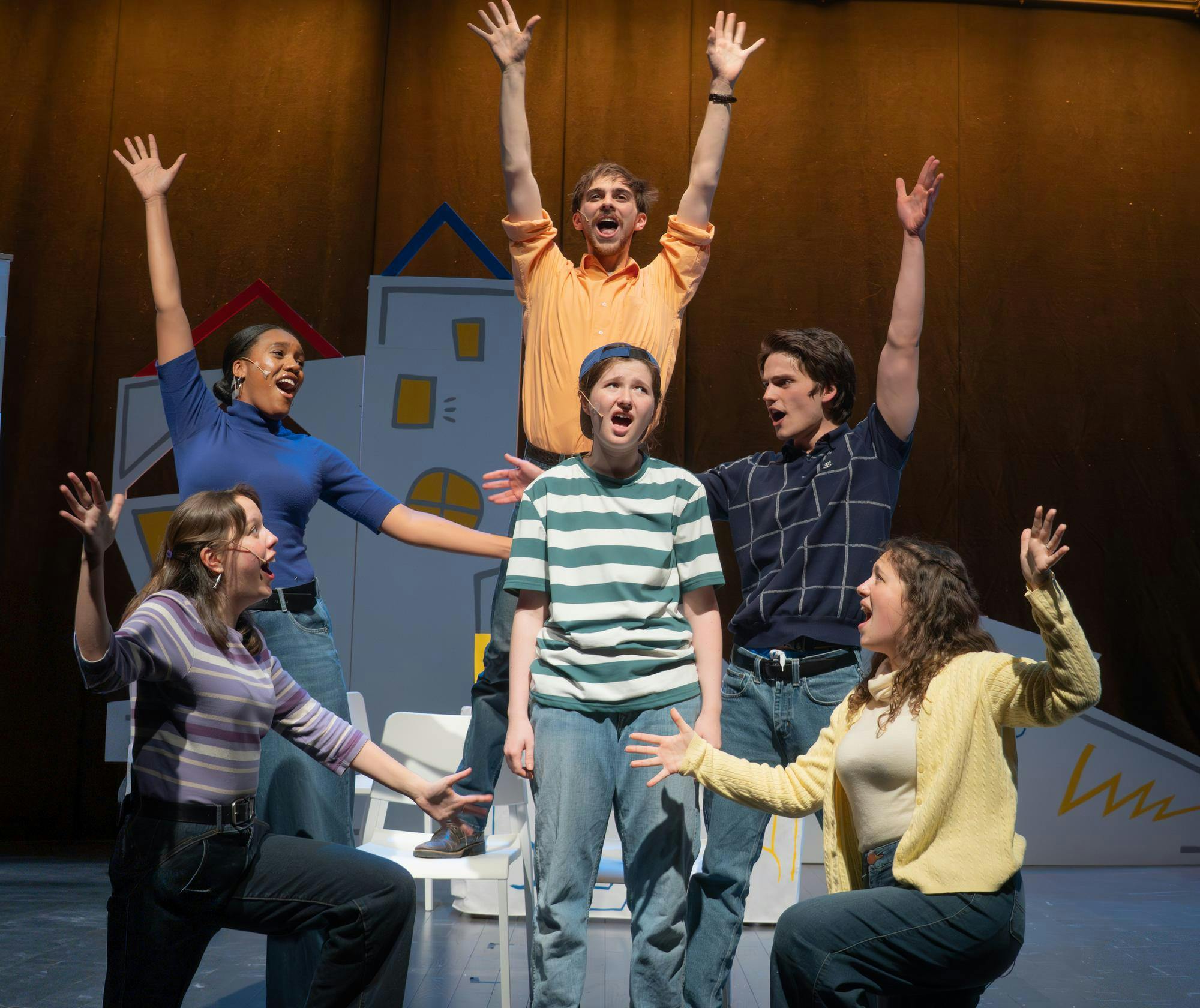 Five stage performers happily surround a sixth performer with a unhappy facial expression. 