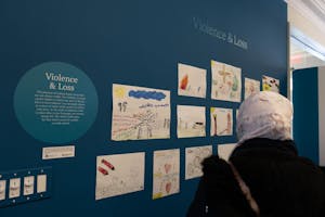 Photo of a woman in a head covering looking at children’s artwork on a wall.

