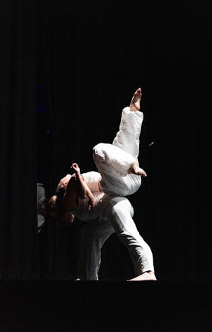Two dancers in all white back to back with one balancing the other. 