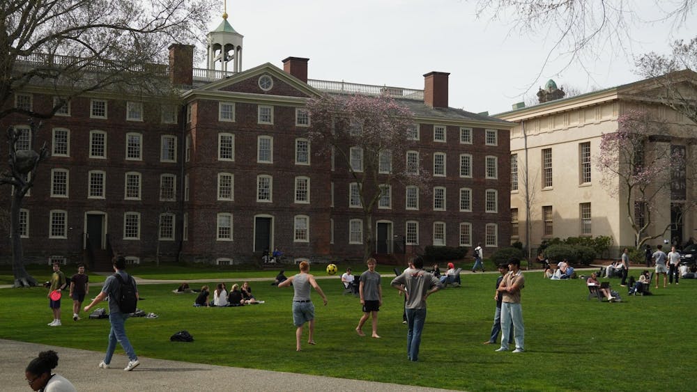 A photo of the Main Green with University Hall in the background. A group of students are playing with a soccer ball while others are sitting on chairs and blankets. 