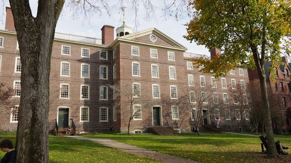 Photo of the University Hall with surrounding trees, pathways around the front yard and multiple students scattered around. 