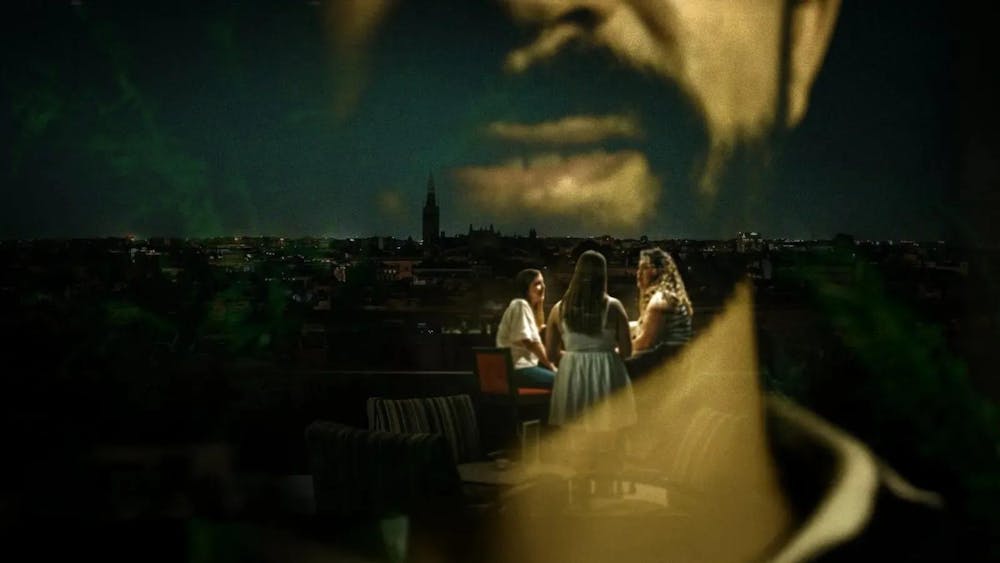 A photo of women at a table with a city in the background is double-exposed with a photo of a man's face. 
