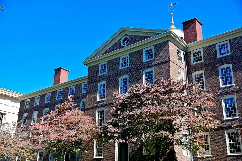 A photo of the back of Brown University’s University Hall, a large brick building, with thick trees of pink flowers in front.