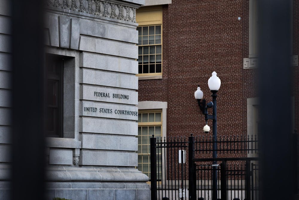 Photo of the U.S. District Court of Rhode Island viewed through two black fence bars. Signage on the courthouse wall reads "Federal Building United States Courthouse."