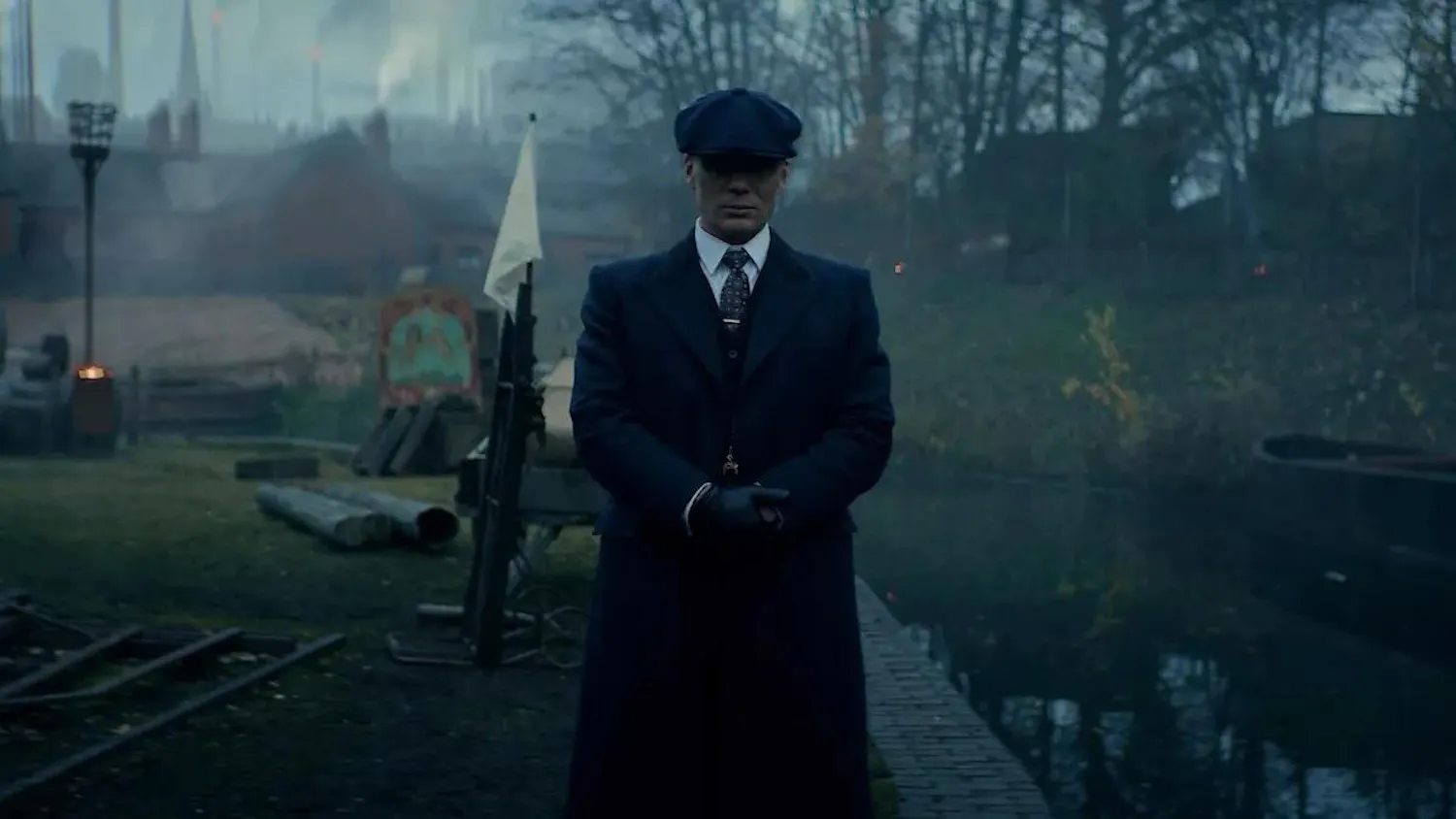 Photo of Tommy Shelby (Cillian Murphy) from Peaky Blinders in a long navy trench coat and cap.