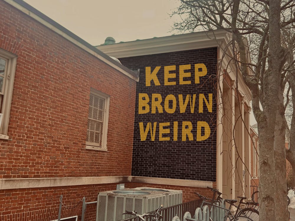 A photo showing a brick wall of the Sharpe Refectory building with the text “Keep Brown Weird” digitally drawn in yellow letters on a black background on it. 