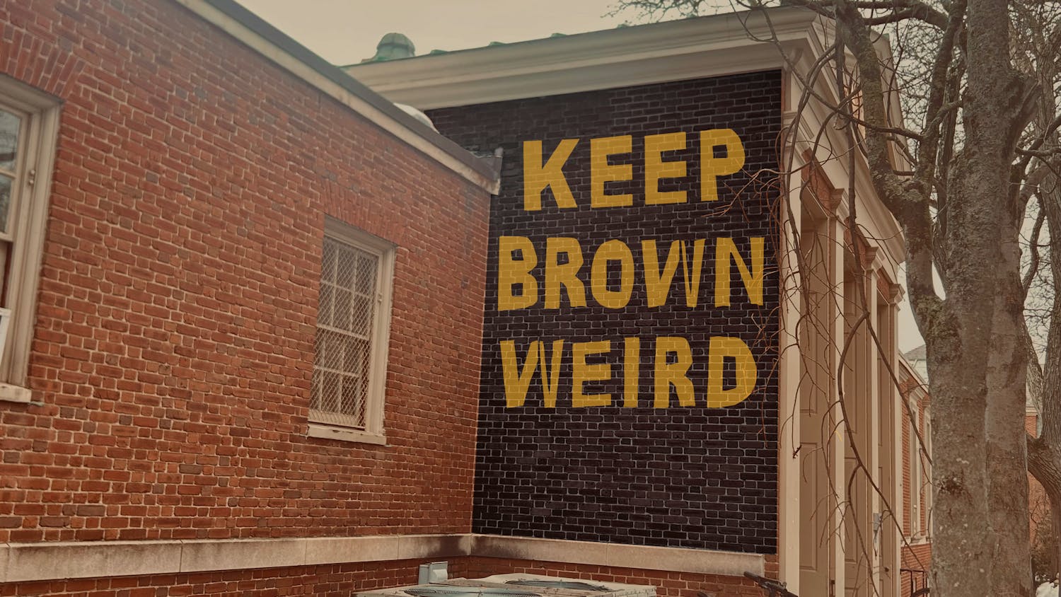 A photo showing a brick wall of the Sharpe Refectory building with the text “Keep Brown Weird” digitally drawn in yellow letters on a black background on it.
