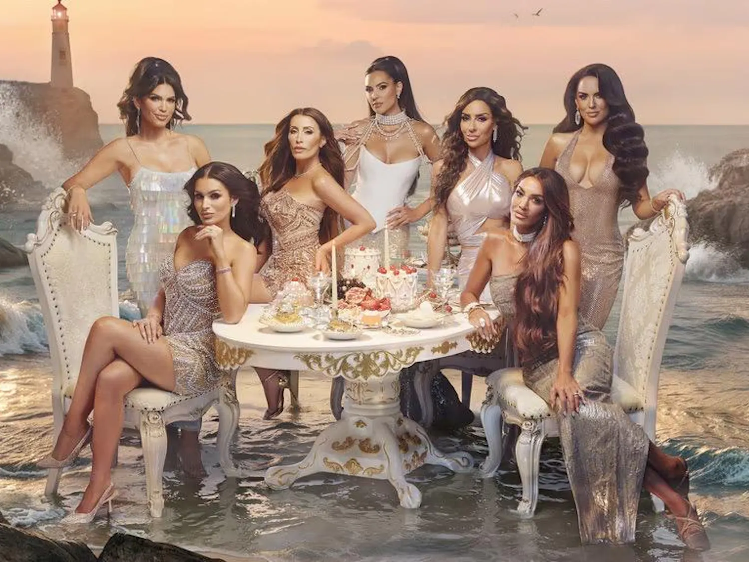 This photo shoes the Real Housewives of Rhode Island in shimmering dresses and sit around a table full of extravagant cakes and a coast is in the background with a lighthouse.