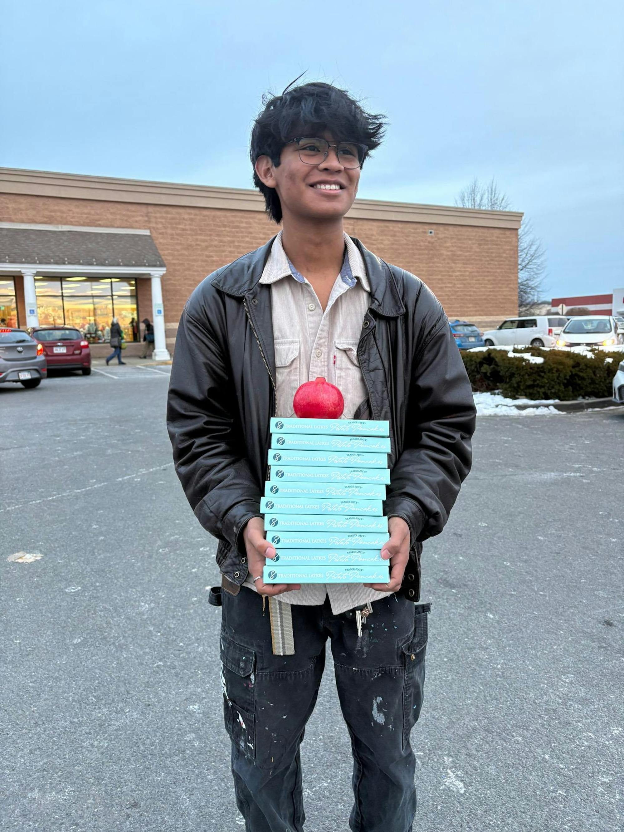 A boy with dark hair stands in front of a brick building. 