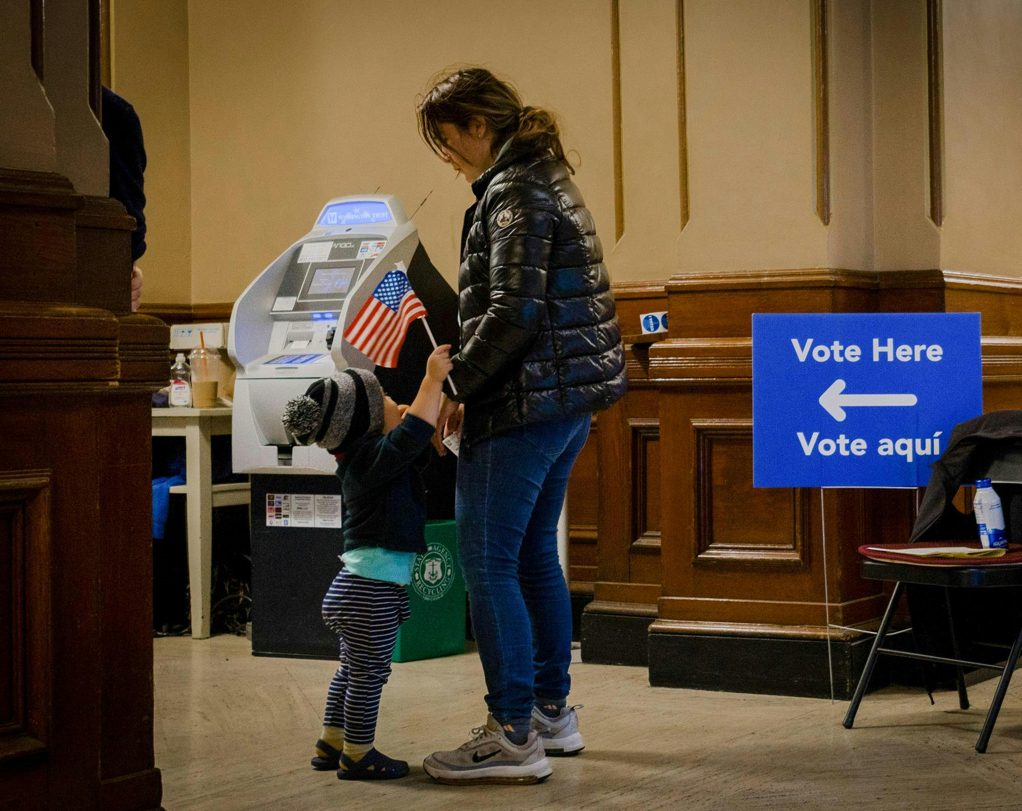 A kid holding an American flag clings onto their mother.