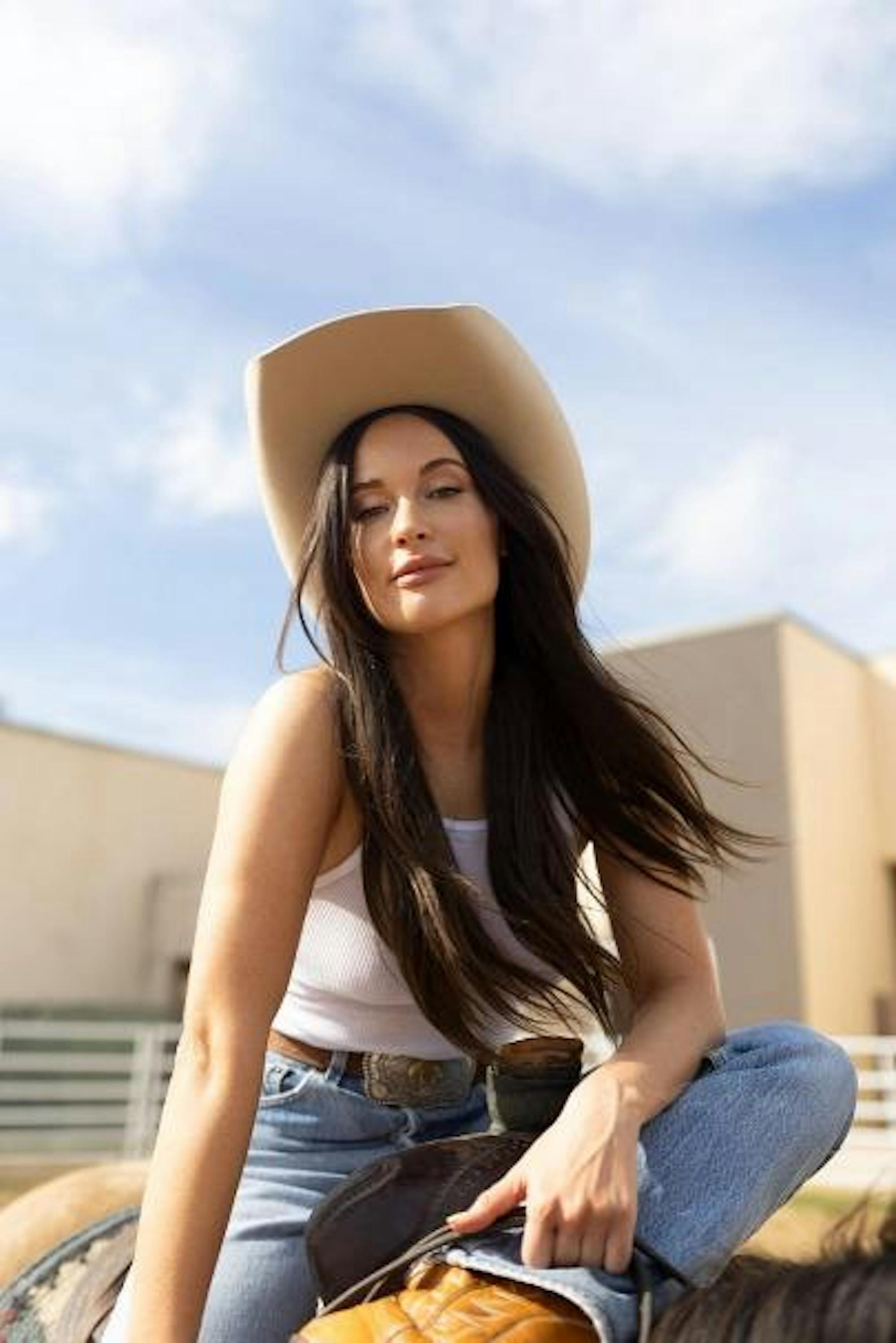 Image of Kacey Musgraves in a cowboy hat looking down at the camera while smirking.
