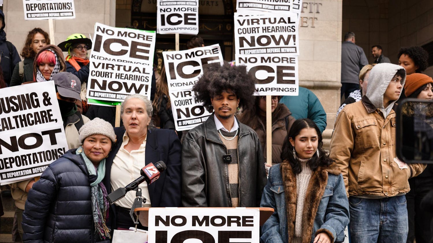 A group of people in front of a podium outside the courthouse. Signs reading "No more ice."