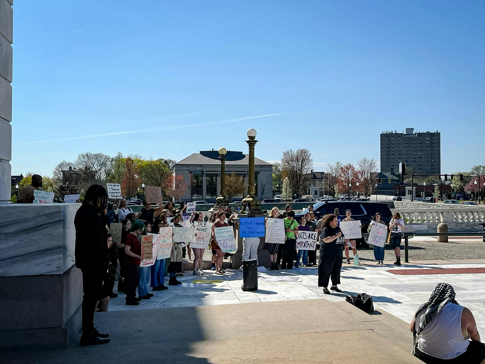 A group of protesters stand holding signs outside of the Rhode Island state house.