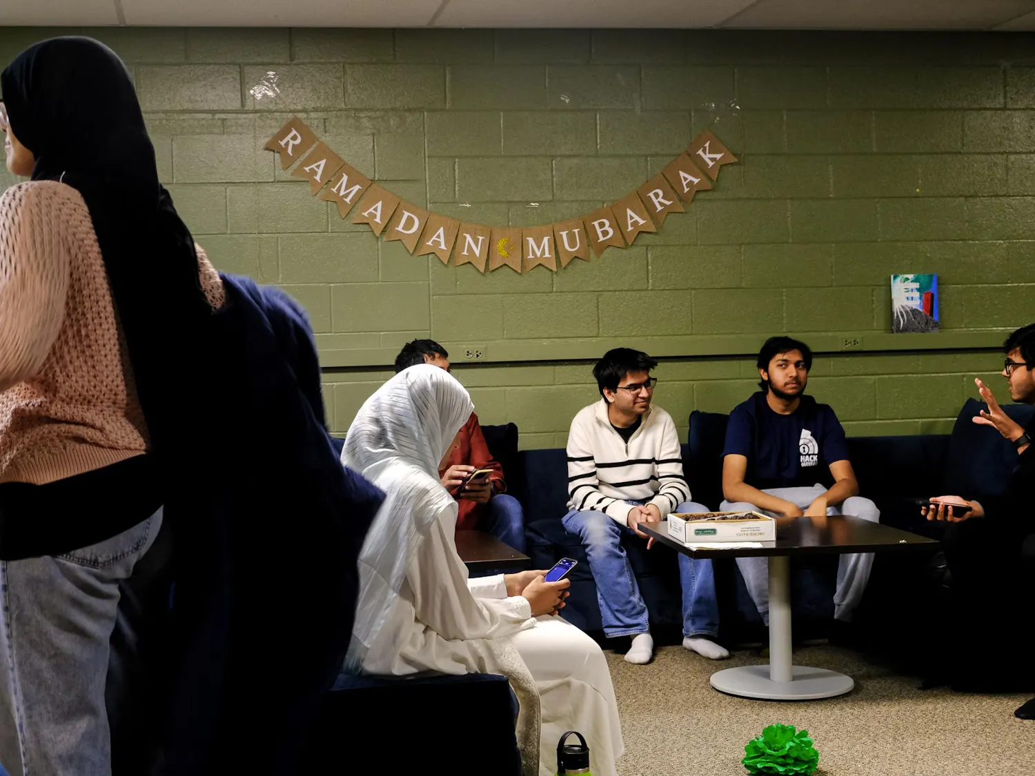 People are sitting together in front of a banner that says "Ramadan Mubarak."