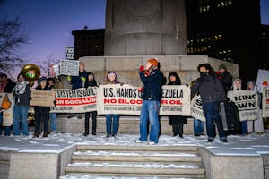 Protestors at night. One person talks into a microphone while others stand behind, holding signs and banners.