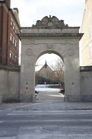 Photo shows archway that opens up onto a snow-covered quiet green. 