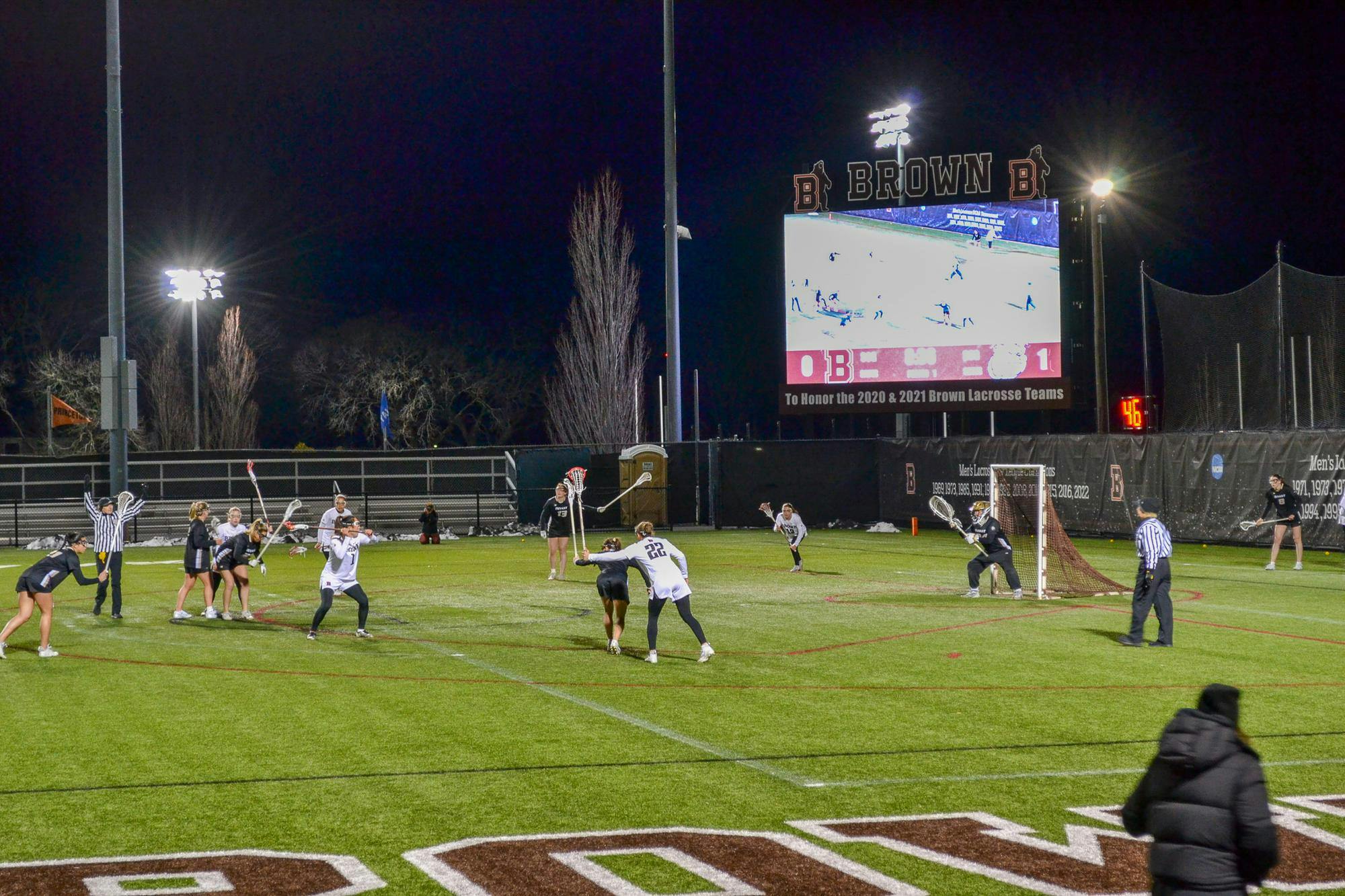 Image of players on a lacrosse field at night in front of a Jumbotron.
