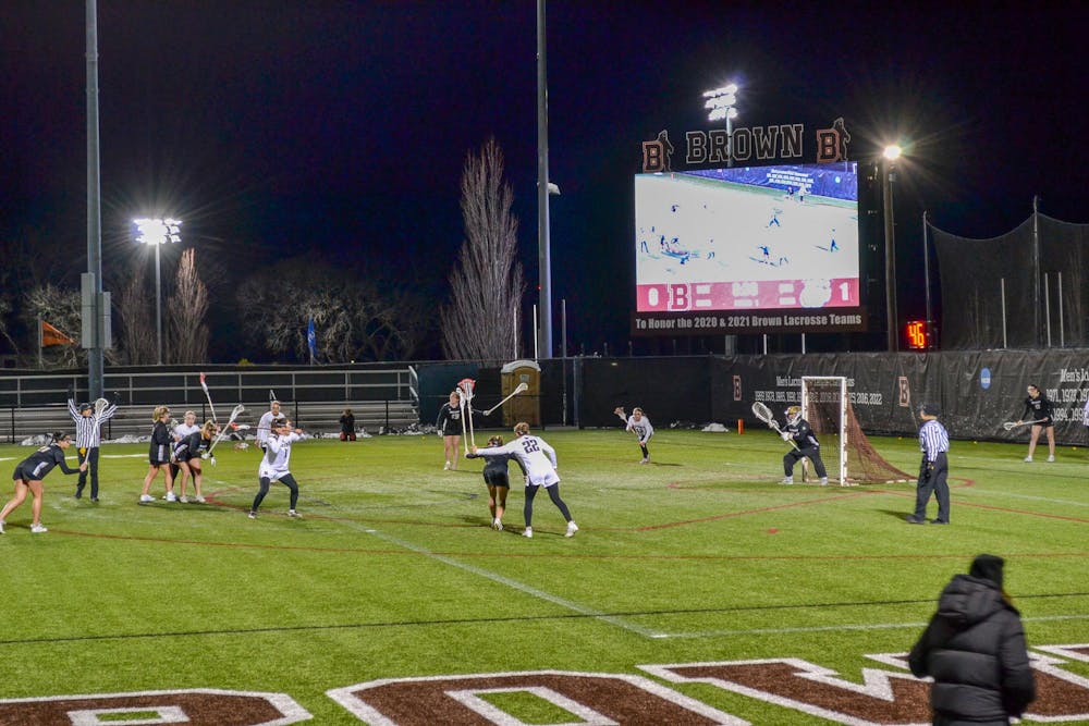 Image of players on a lacrosse field at night in front of a Jumbotron.