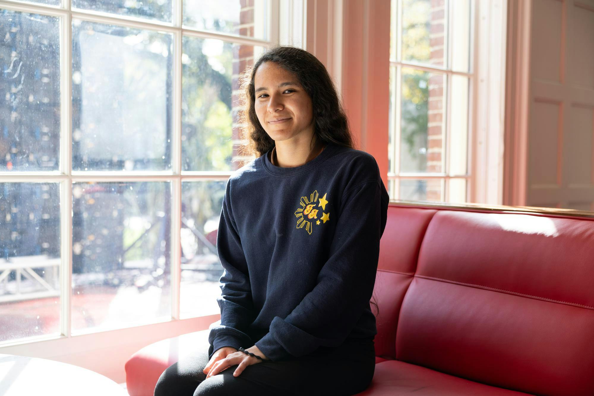 A woman sits at a window, smiling at the camera.