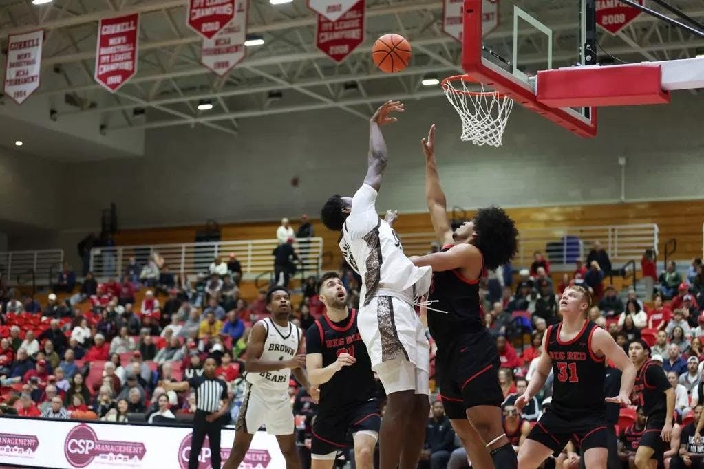 Photo of a Brown player midair shooting the ball toward the net while a Cornell player attempts to block it. 