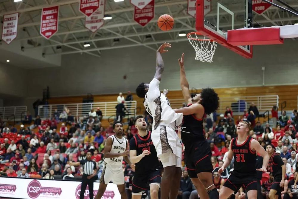 Photo of a Brown player midair shooting the ball toward the net while a Cornell player attempts to block it. 