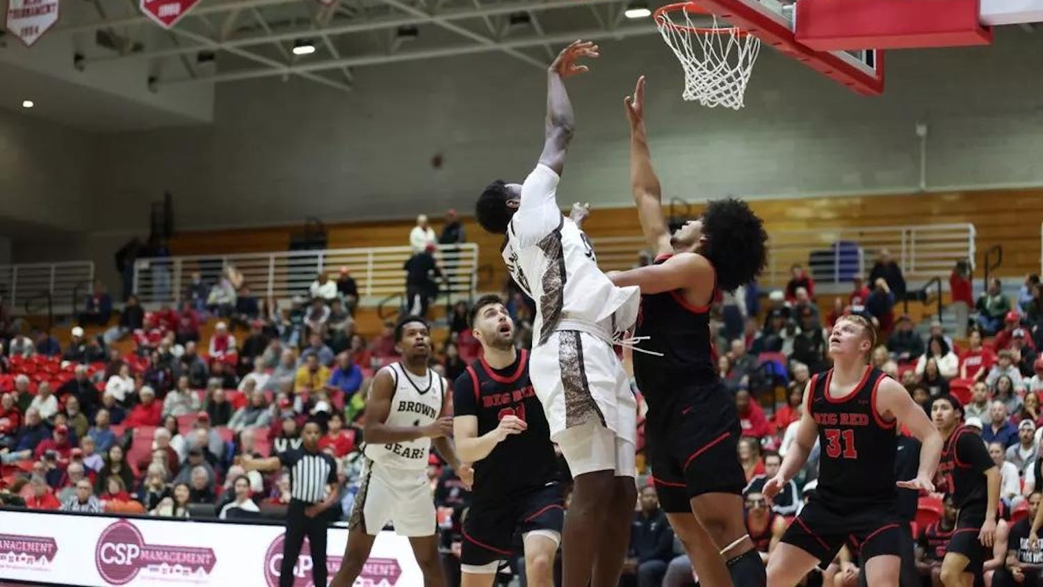 Photo of a Brown player midair shooting the ball toward the net while a Cornell player attempts to block it.
