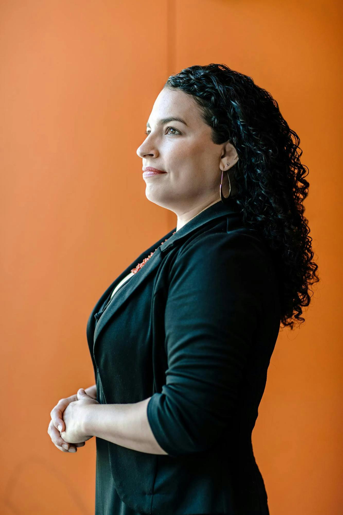 A profile portrait photo of Professor Nicole Gonzalez Van Cleve against an orange background. She is wearing a black jacket and looking into the distance.