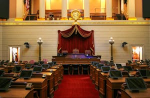 Courthouse with several wooden tables on the left and right with tablets and voting button sets. In the center is a red carpeted walkway with a large table in the center with red curtains.