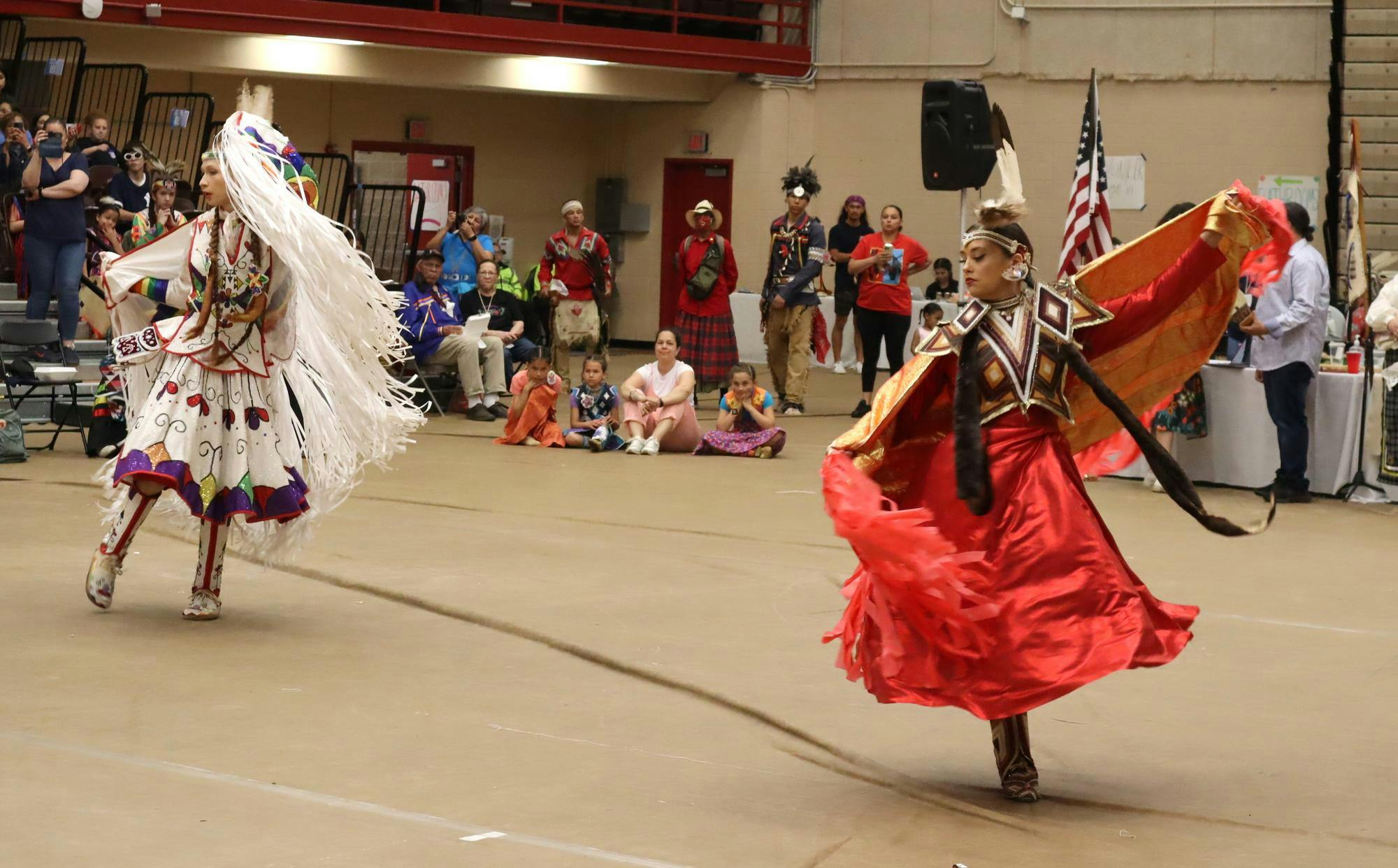 A photo of two Native American women in traditional dress dancing at the Pizzitola Sports Center.